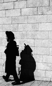 Side view of man walking on footpath by wall