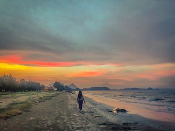 Rear view of people standing on beach against sky during sunset