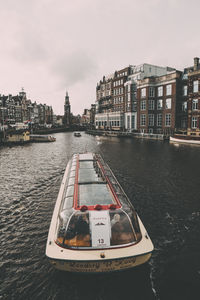 Boat in canal by buildings against sky in city