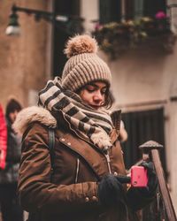 Young woman using mobile phone in city during winter