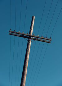 Low angle view of electricity pylon against clear blue sky
