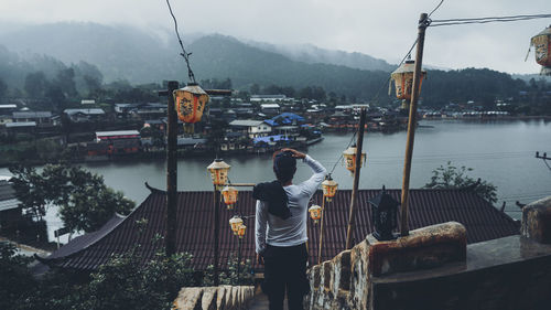 Rear view of man looking at cityscape by river against mountains