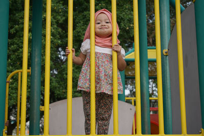 Portrait of smiling girl in hijab standing by yellow play equipment
