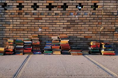 Stack of books on footpath against brick wall