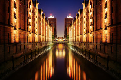 Canal amidst illuminated buildings in city at night