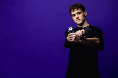 Portrait of young barber standing against blue background