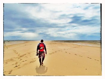 Rear view of man standing on beach against cloudy sky