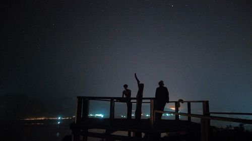 Silhouette people standing by railing against sky at night