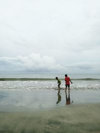 Rear view of men on beach against sky