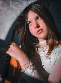 Beautiful young woman looking away while holding violin