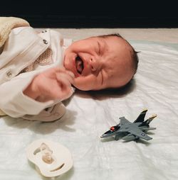 Close-up of crying baby with airplane toy on bed