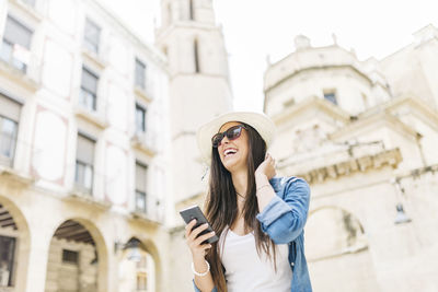 Low angle view of young woman using mobile phone in city