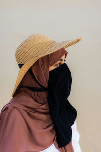 Close up head shot of muslim girl wearing hat, niqab, and hijab against bright yellow background