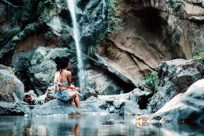 Full length of shirtless man standing on rocks at shore