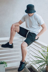 Full length of man sitting on railing against wall