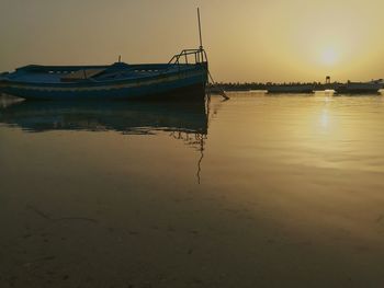 Sailboats moored on sea against sky during sunset