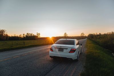 Cars on road amidst field against sky during sunset