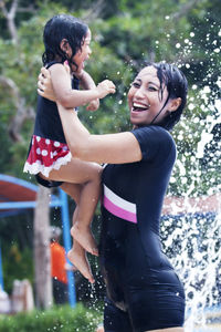 Smiling mother carrying daughter against fountain