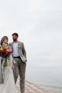 Newly married couple walking on pier over lake against cloudy sky