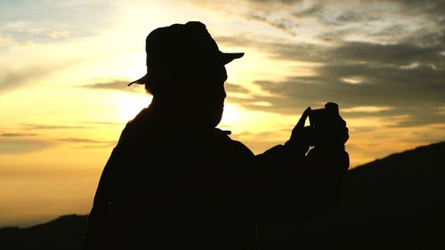 Silhouette man holding orange while standing against sky during sunset