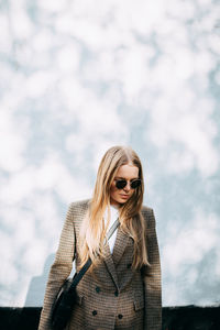 Young woman wearing sunglasses standing against sky