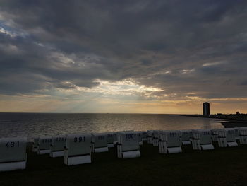 Hooded chairs on beach against sky during sunset