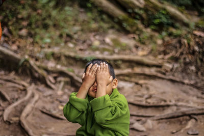 Close-up of boy with hands covering eyes sitting on land