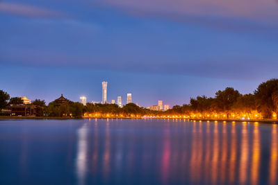 Illuminated buildings by lake against blue sky