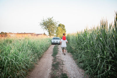 Father holding child on the shoulders walks away on country road to car