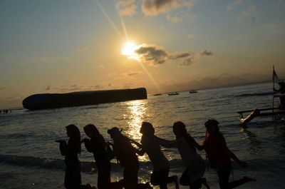 Silhouette people on beach against sky during sunset