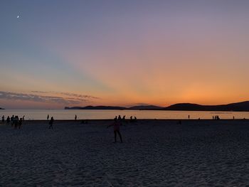 Silhouette people on beach against sky during sunset