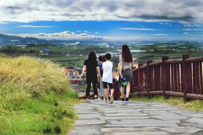 Rear view of women walking on footpath against sky