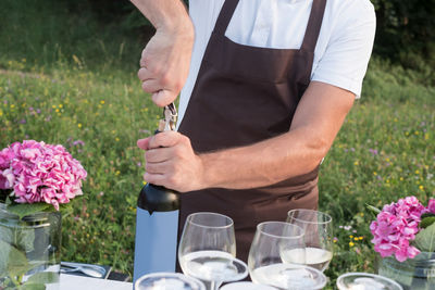 Midsection of man opening wine bottle while standing at yard