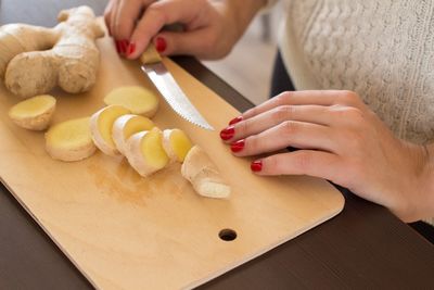 Cropped hands of woman cutting ginger on board in kitchen at home