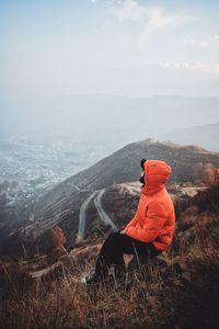 Man sitting on mountain against sky