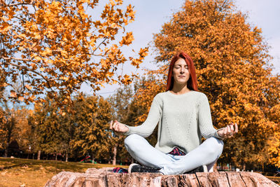 Full length of woman doing yoga while sitting against trees during autumn