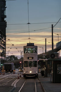 Cars on city street against sky at sunset