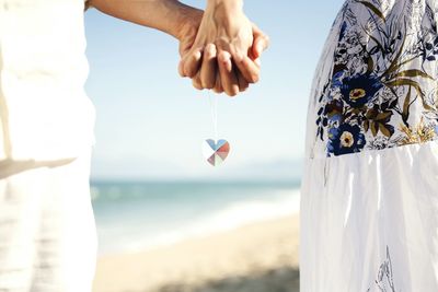 Midsection of couple holding hands with love locket chain at beach