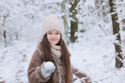 Portrait of a smiling girl in snow, holding a snowball in her hand