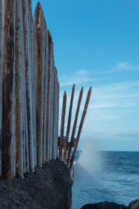 Wooden posts in sea against blue sky