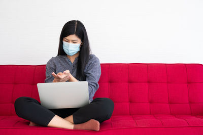 Young woman using phone while sitting on laptop