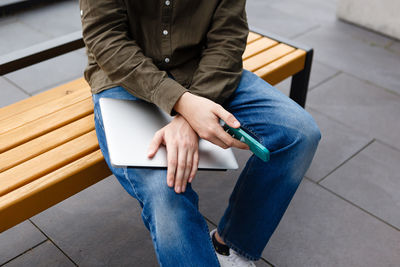 Man holding a laptop and a smartphone while sitting on a bench