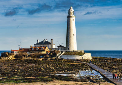 Lighthouse by sea against sky during sunset