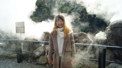 Portrait of woman standing against trees and smoke