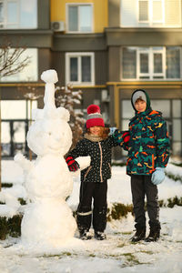 Winter portrait of children with a plastic sled sliding on a snowy slope and making a snowman