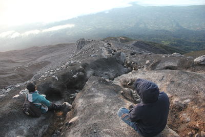 Rear view of men sitting on rock