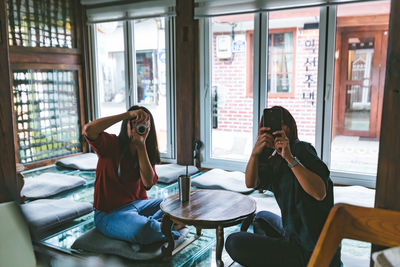 Young woman photographing while sitting on table at home