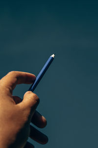 Midsection of person holding umbrella against blue sky