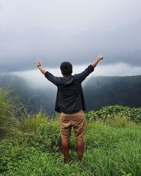 Rear view of man standing on mountain against sky