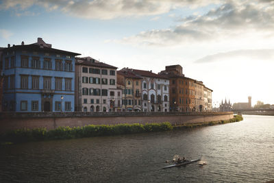 View of buildings by river against cloudy sky